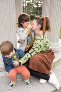 A mom is booped on the nose by her older son as her younger son attempts to wiggle away